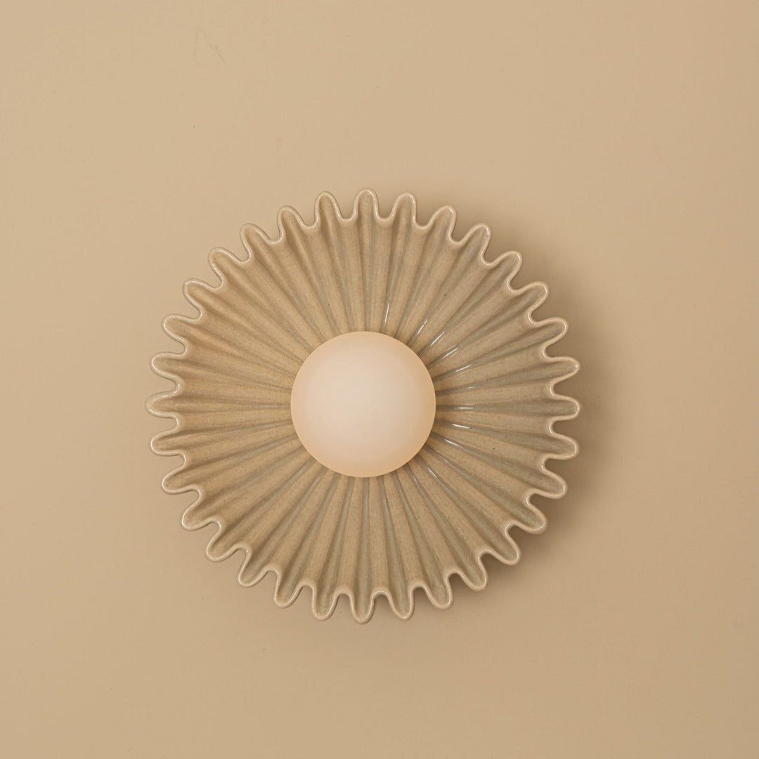 Sea-colored wall light by Simone and Marcel, featuring a wavy, scalloped edge and a central, spherical bulb.