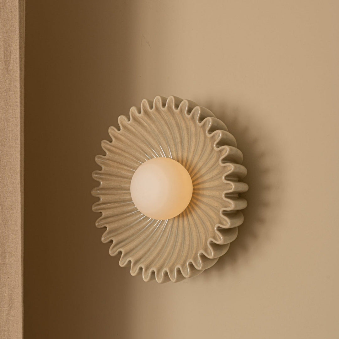 Sea wall light by Simone and Marcel with a ruffled, ceramic shade and a central, glowing bulb.