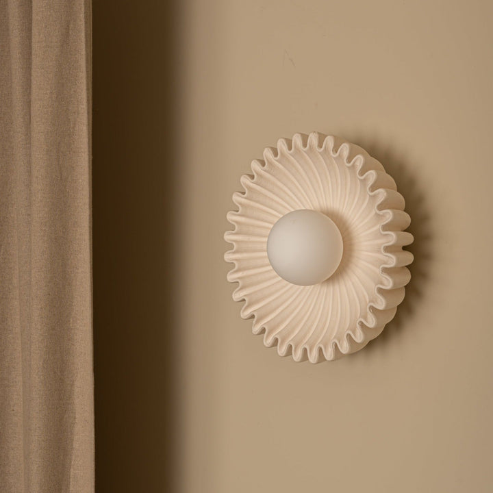 A Simone and Marcel wall-mounted ceramic Ostro lamp with an ecru matte glaze, featuring a central glass globe, diffusing soft light, against a neutral background from Shop Dessein Parke