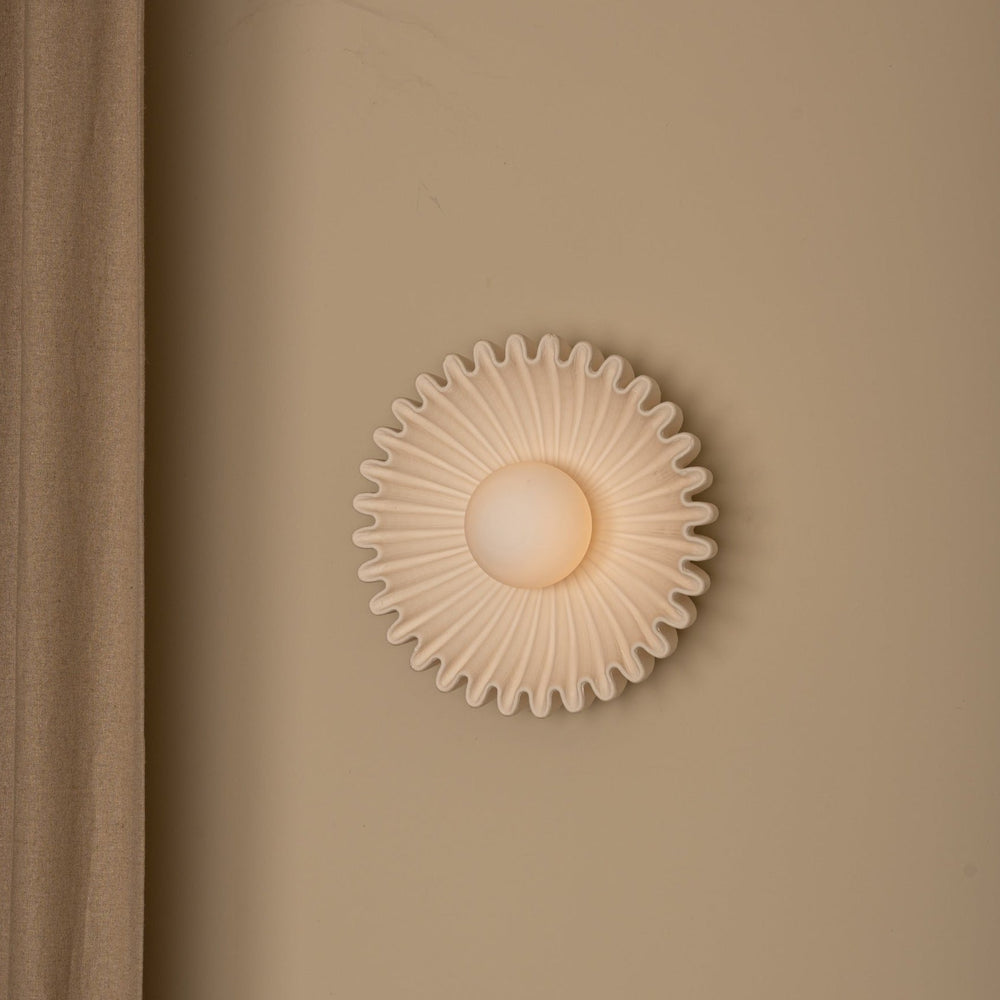 Ecru wall light by Simone and Marcel with a ruffled, flower-like shape on a beige wall.