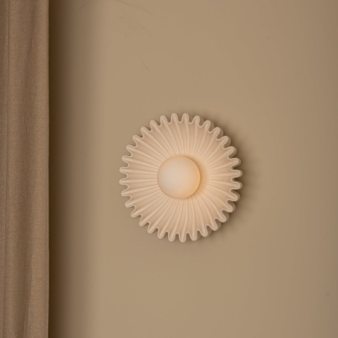 Ecru wall light by Simone and Marcel with a ruffled, flower-like shape on a beige wall.