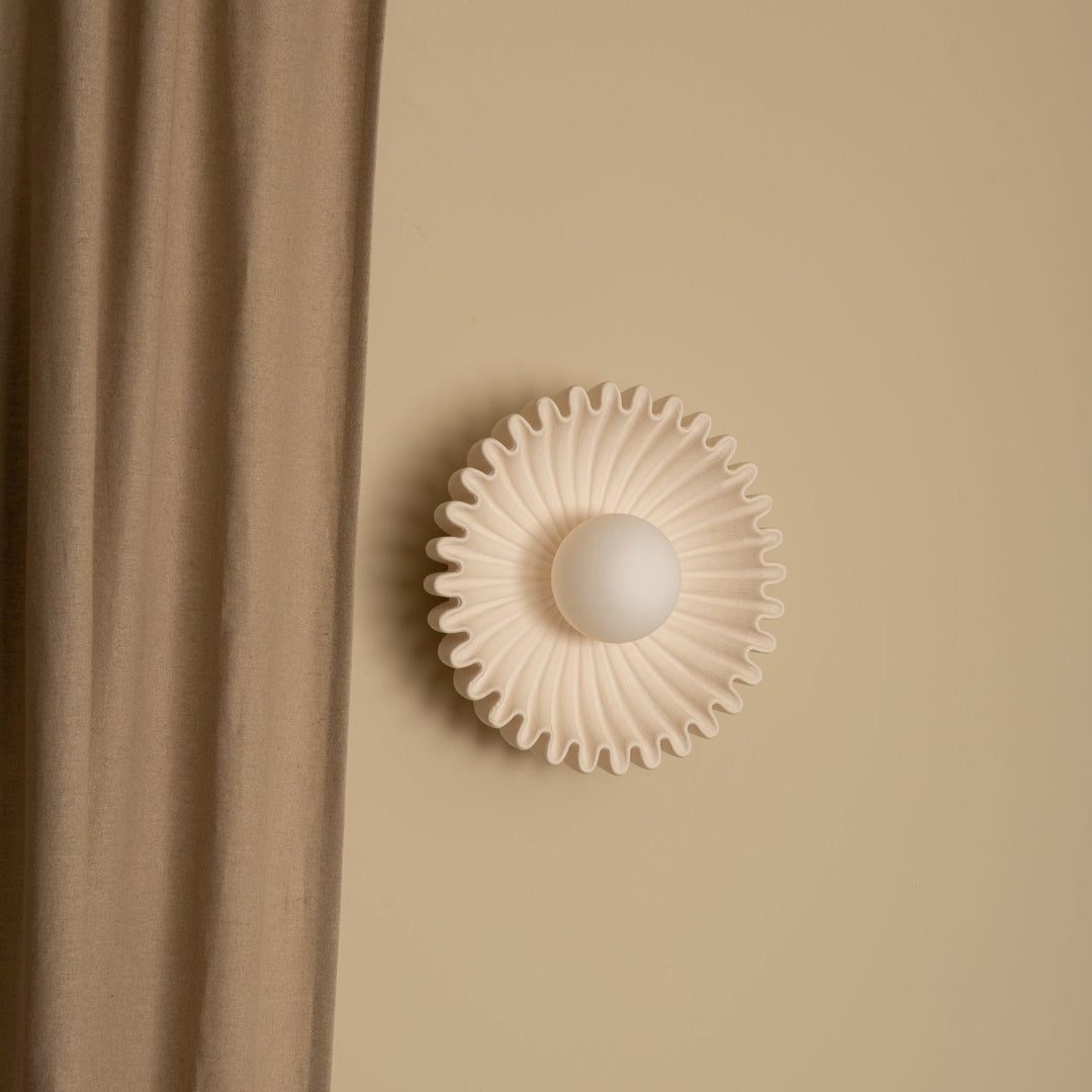Ecru wall light by Simone and Marcel with a round, globe-shaped bulb and a ruffled shade.