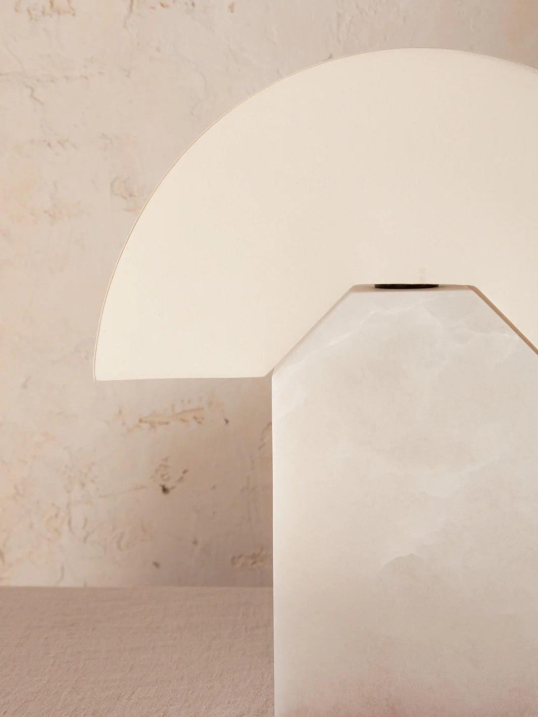 Alabaster table lamp by Simone and Marcel with a rounded shade against a textured wall.