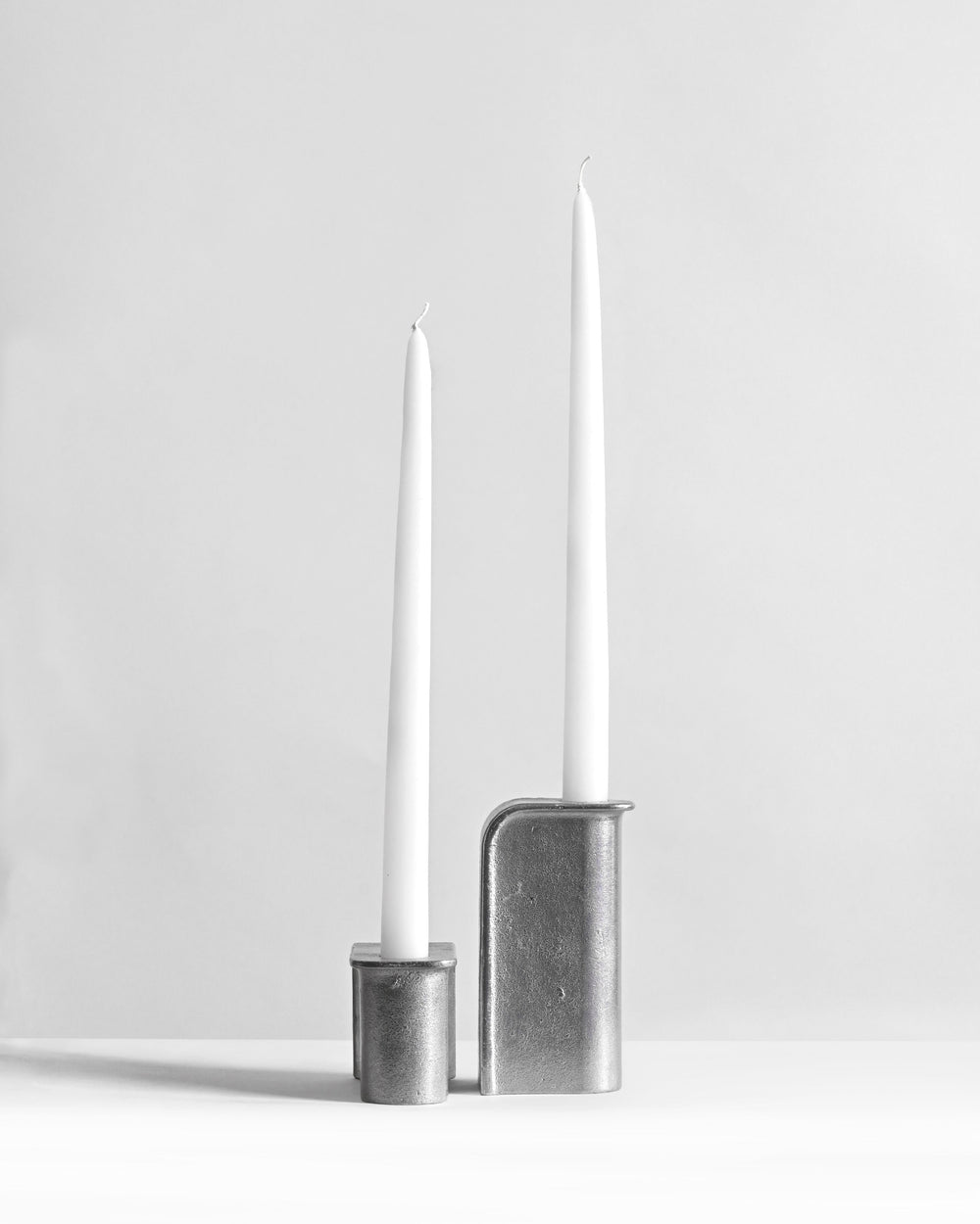 Two tall white candles in metallic candle holders on a light gray background