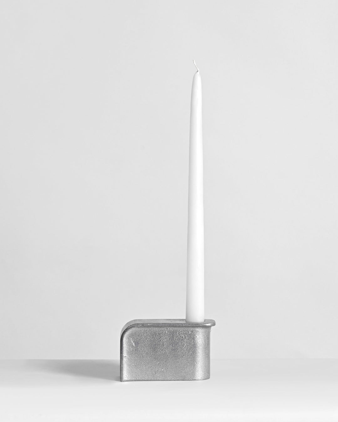 Silver candle holder with a white candle on a light gray background