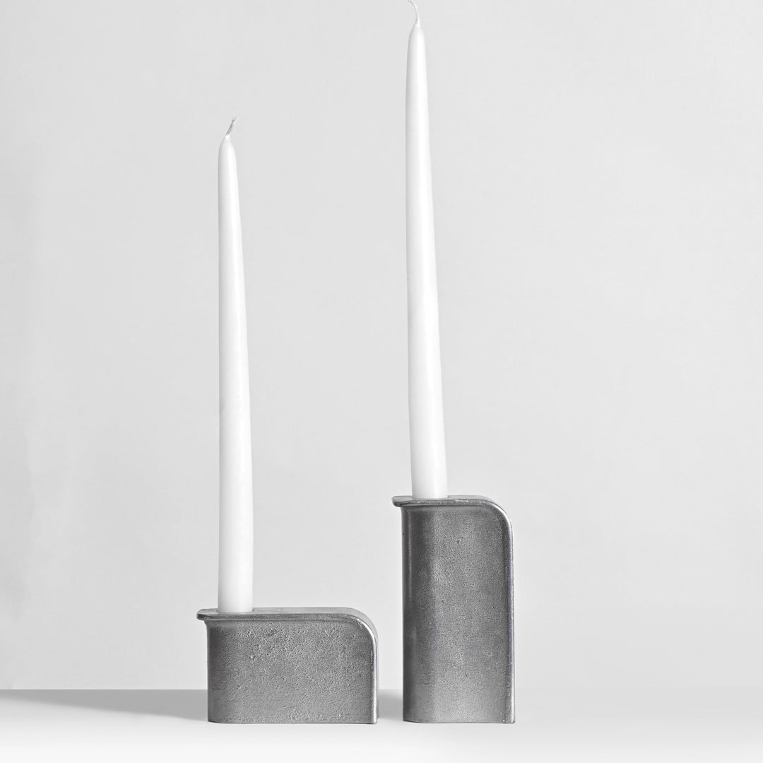 Two gray candle holders with white candles on a light gray background