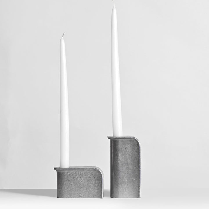 Two gray candle holders with white candles on a light gray background