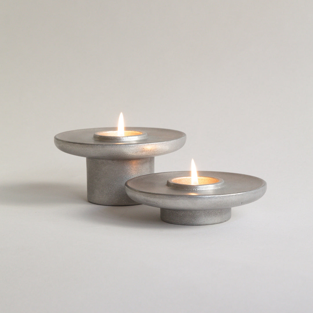 Two metallic candle holders with candles on a light gray background