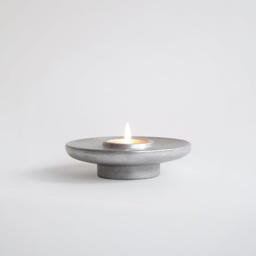 Aluminium candle holder with a lit candle on a white background