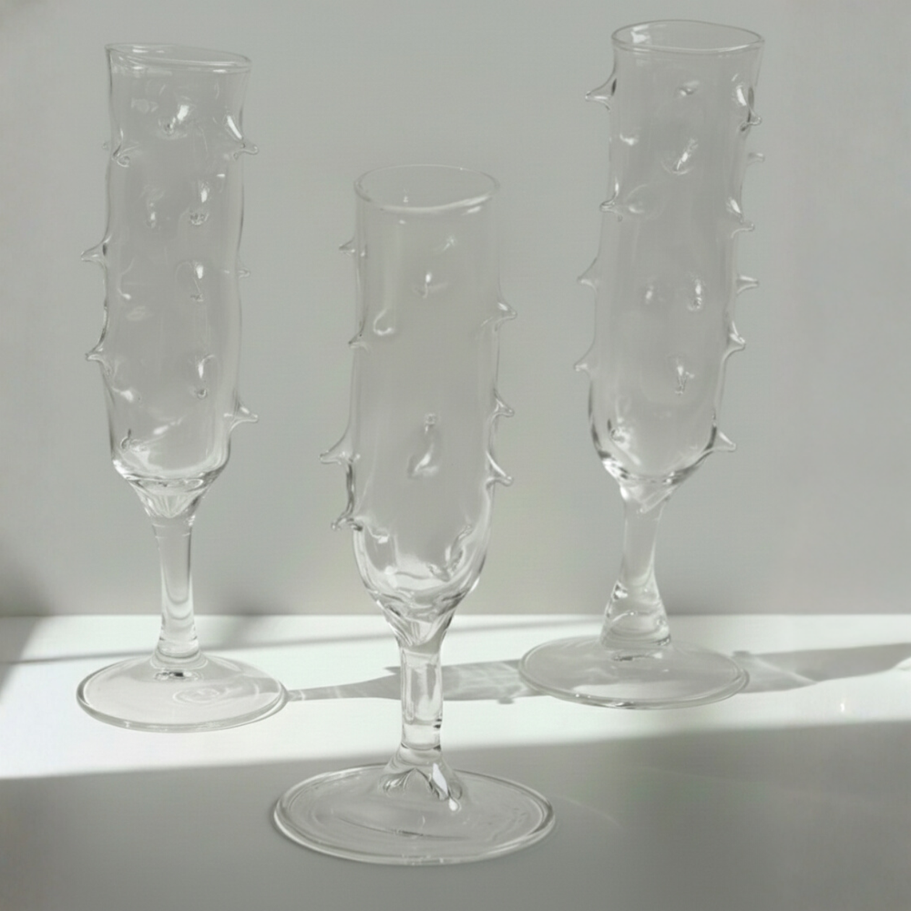 Three clear glass champagne flutes with textured design on a light gray background