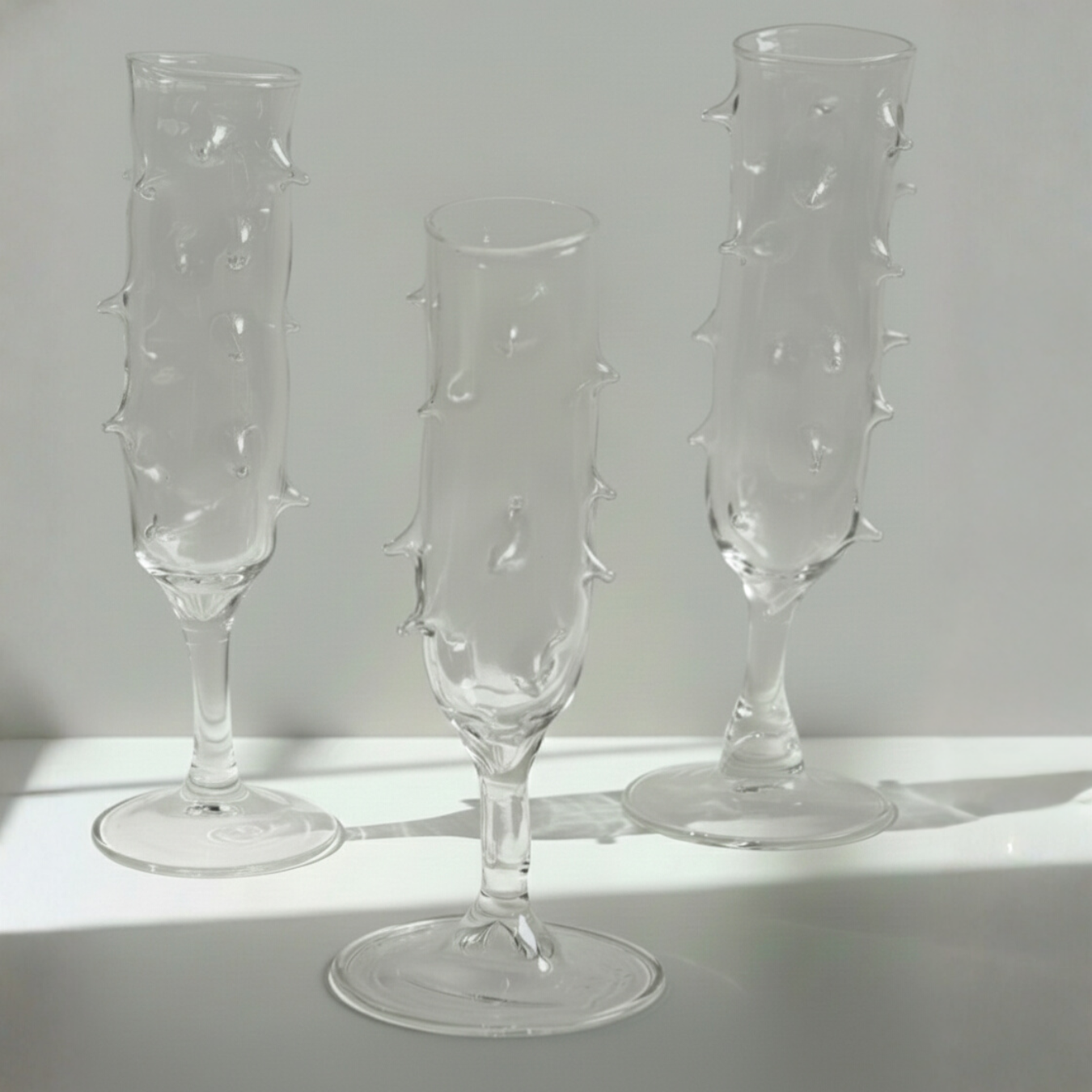 Three clear glass champagne flutes with textured design on a light gray background