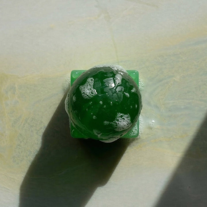 Green sphere soap on a green resin square block against a white background