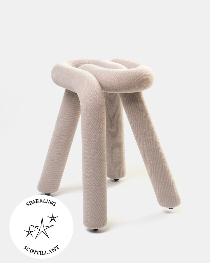 Beige knotted stool by Moustache featuring a soft, textured upholstery and three cylindrical legs with caster wheels.
