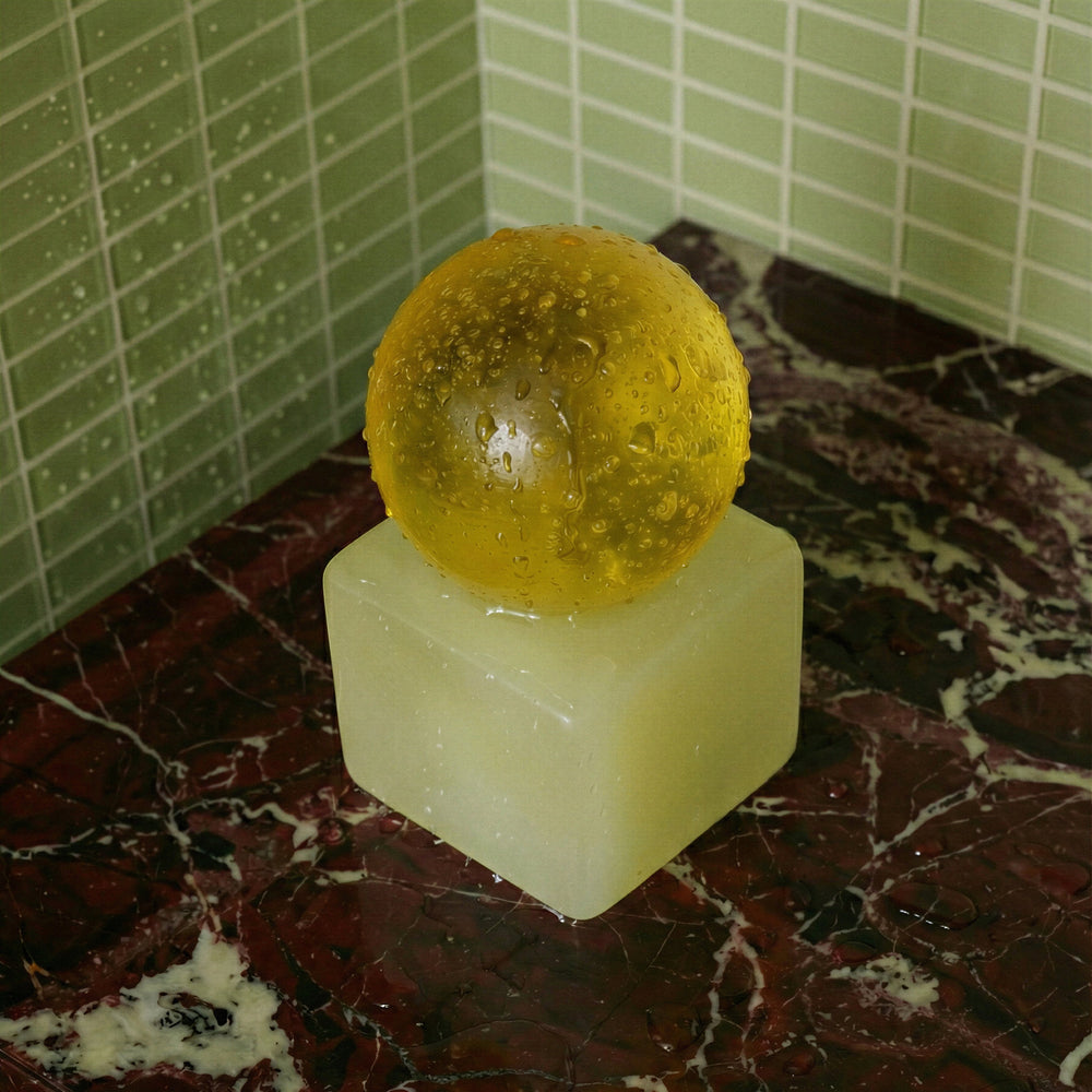 Yellow spherical soap on a square block of resin on a marbled surface with tiled wall background
