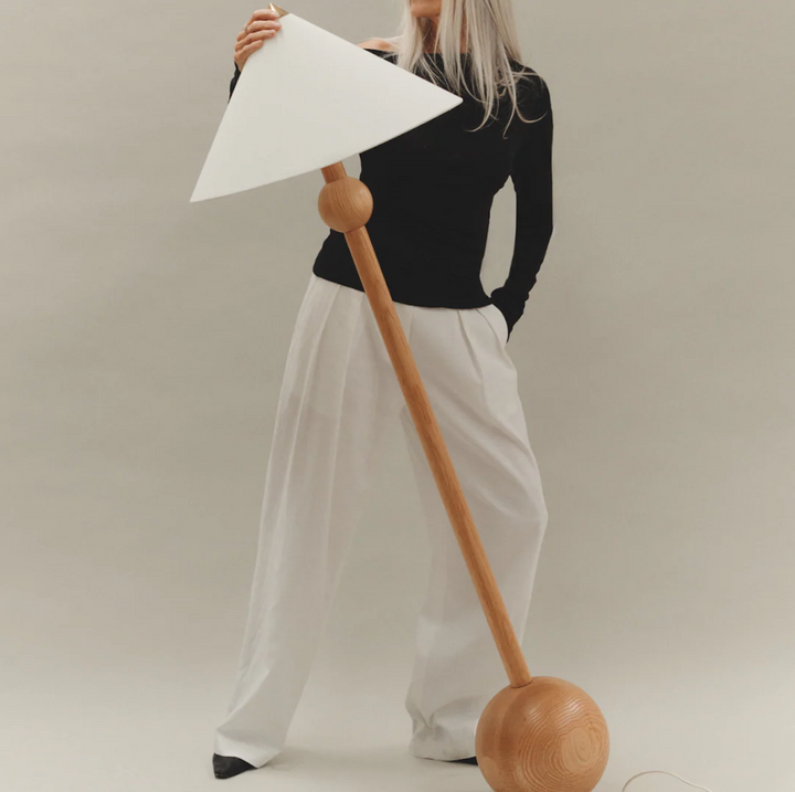 Minimalist floor lamp with a wooden base by McMullin, featuring a white triangular shade.