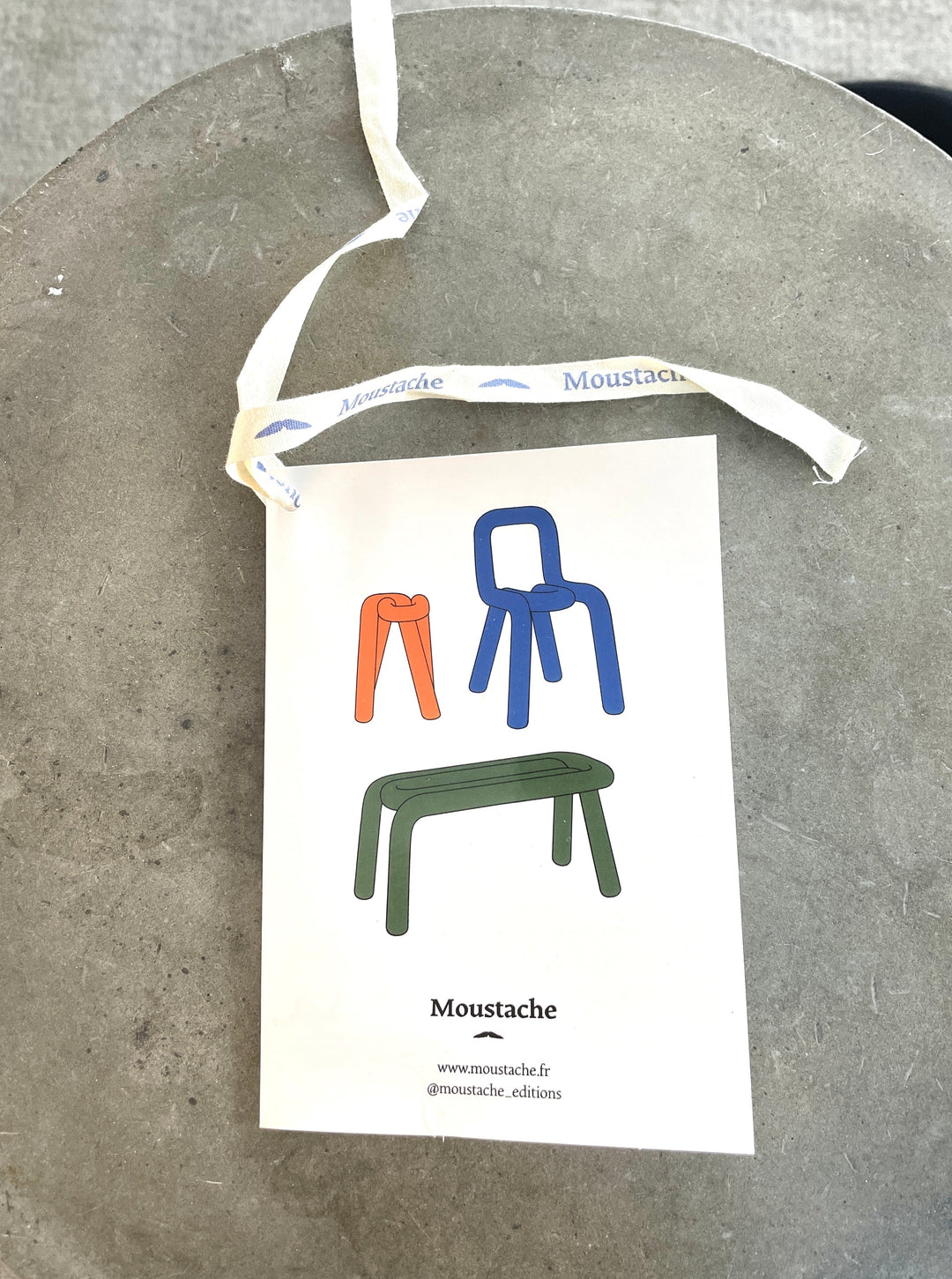 Forest green stool by Moustache, with a printed tag showing colorful chair designs.