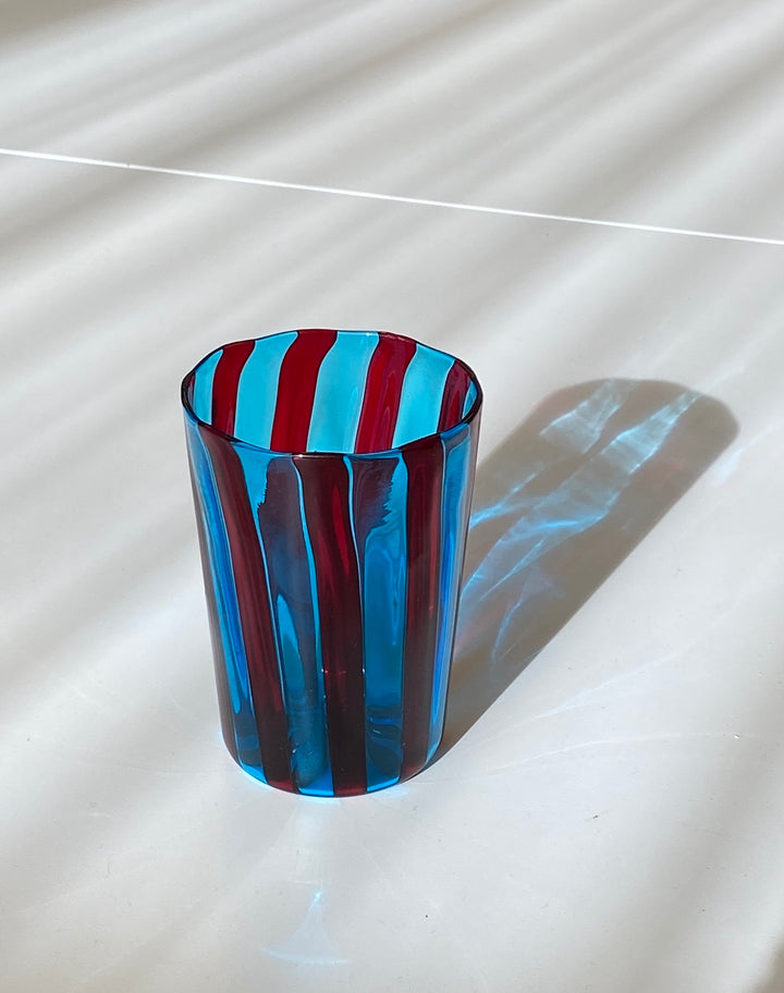 Striped blue and red tumbler by Laguna-B, with a shiny finish and its shadow cast on a white surface.
