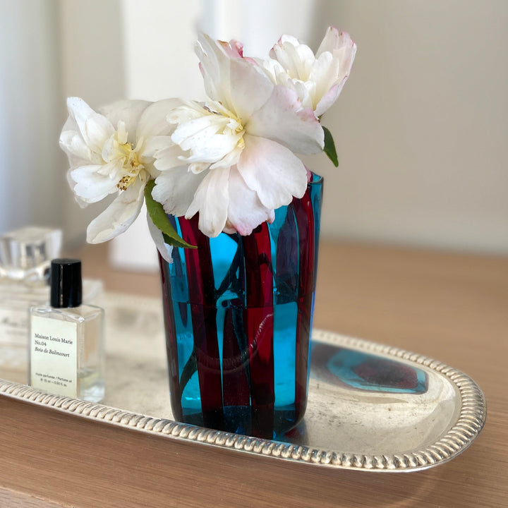 Blue and red murano drinking glass with flowers in it on a sliver tray