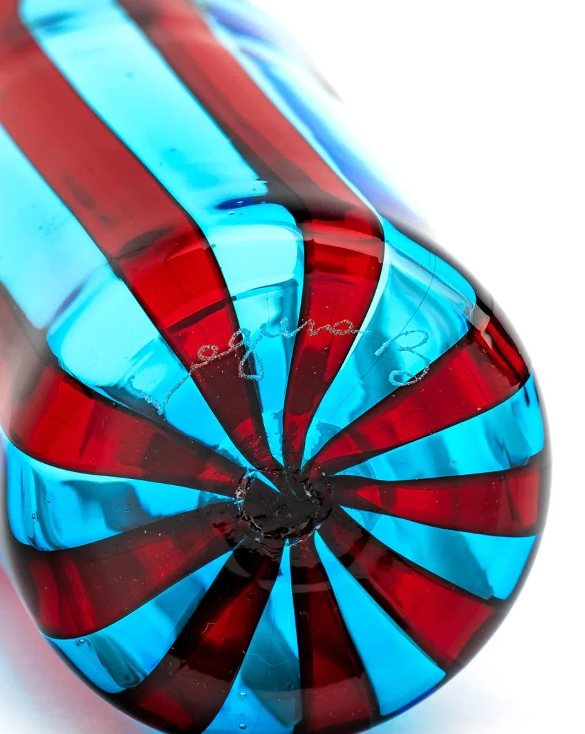 Striped drinking glass by Laguna-B, with red and blue spiraling bands converging at the base, and a signature.