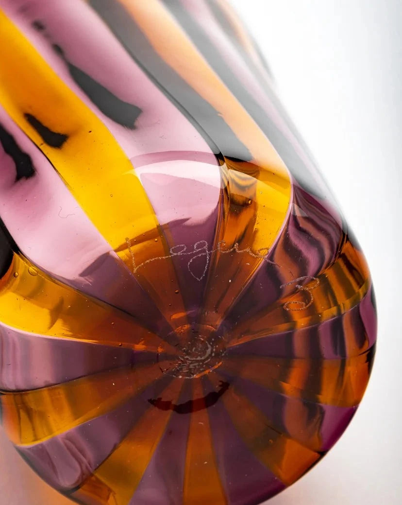 Striped drinking glass by Laguna-B with swirling bands of orange, pink, and black.