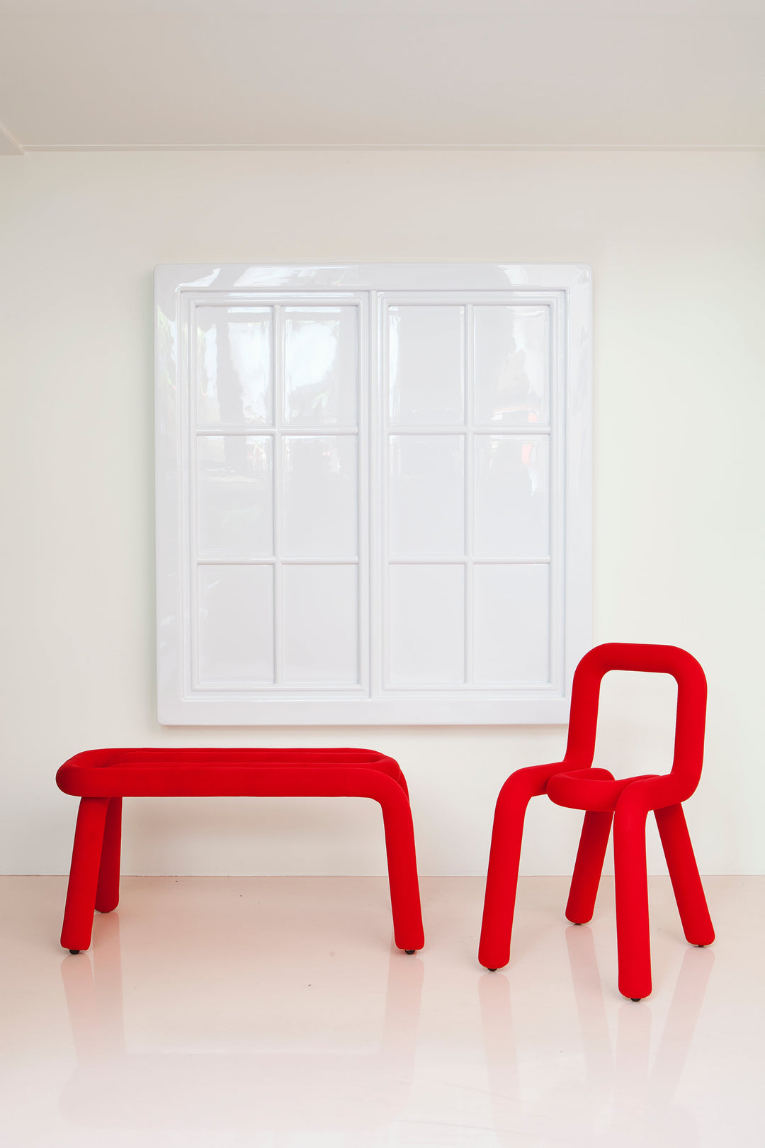 Red bench and chair against a white wall and window.