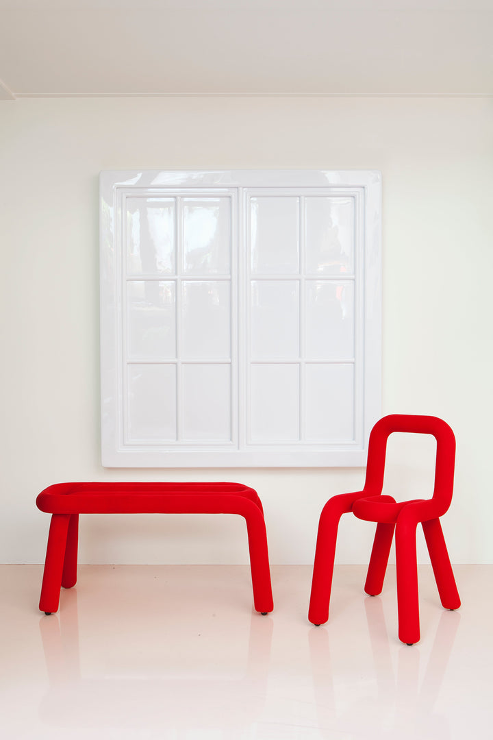 Red bench and chair against a white wall and window.