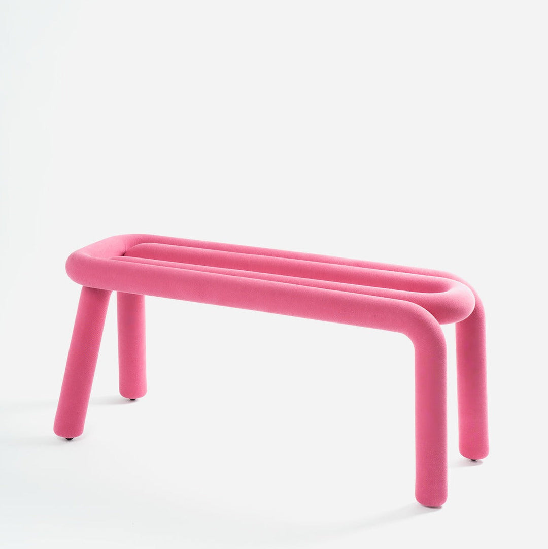 Pink upholstered bench by Moustache Paris with a rounded tubular design and short, cylindrical legs.
