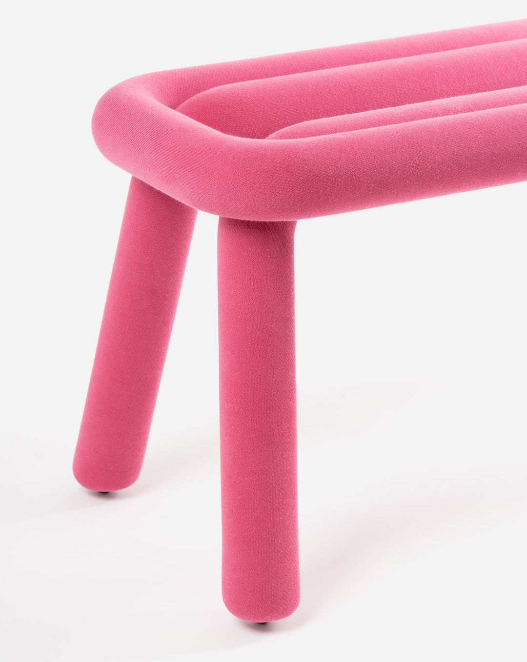 Pink bench by Moustache with soft, rounded lines and tubular legs against a white background.

