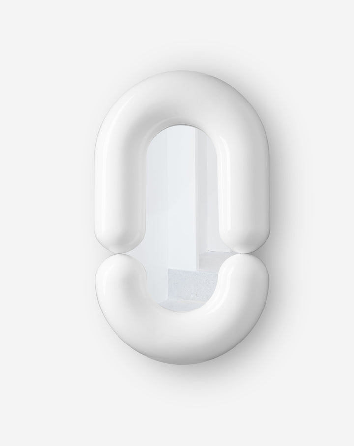 White round wall mirror by Moustache Paris reflecting a white staircase and interior.