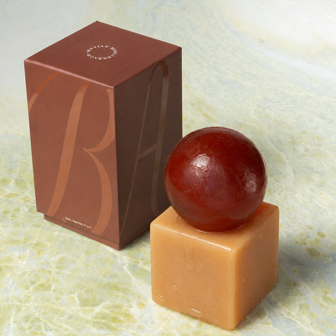Cube-shaped resin with a sphere of soap on top next to a brown box on a marble surface