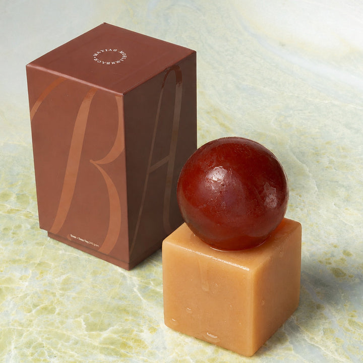 Cube-shaped resin with a sphere of soap on top next to a brown box on a marble surface