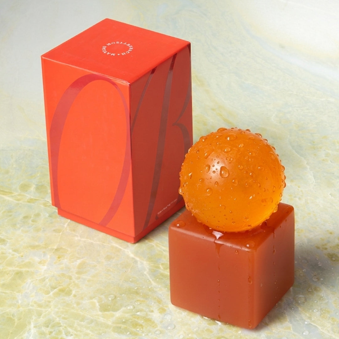 Orange spherical soap on a red stand next to an orange box on a textured surface