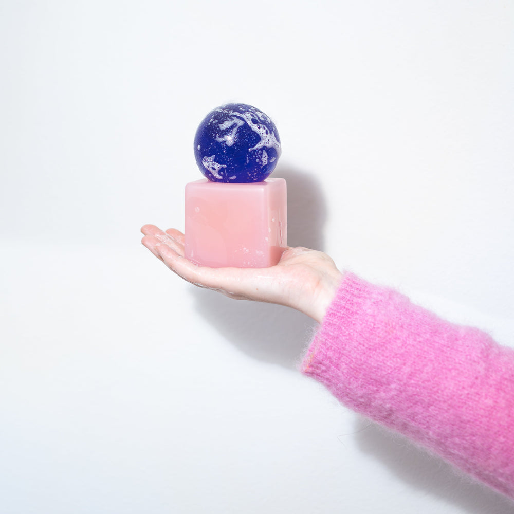 Hand holding a small pink cube with a blue and white sphere on a white background