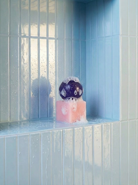 Decorative object with a purple sphere and pink base on a tiled shelf.