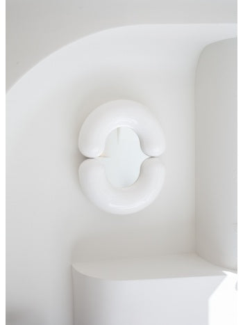 Small white wall mirror by Moustache Paris with a rounded form, mounted on a clean white wall.