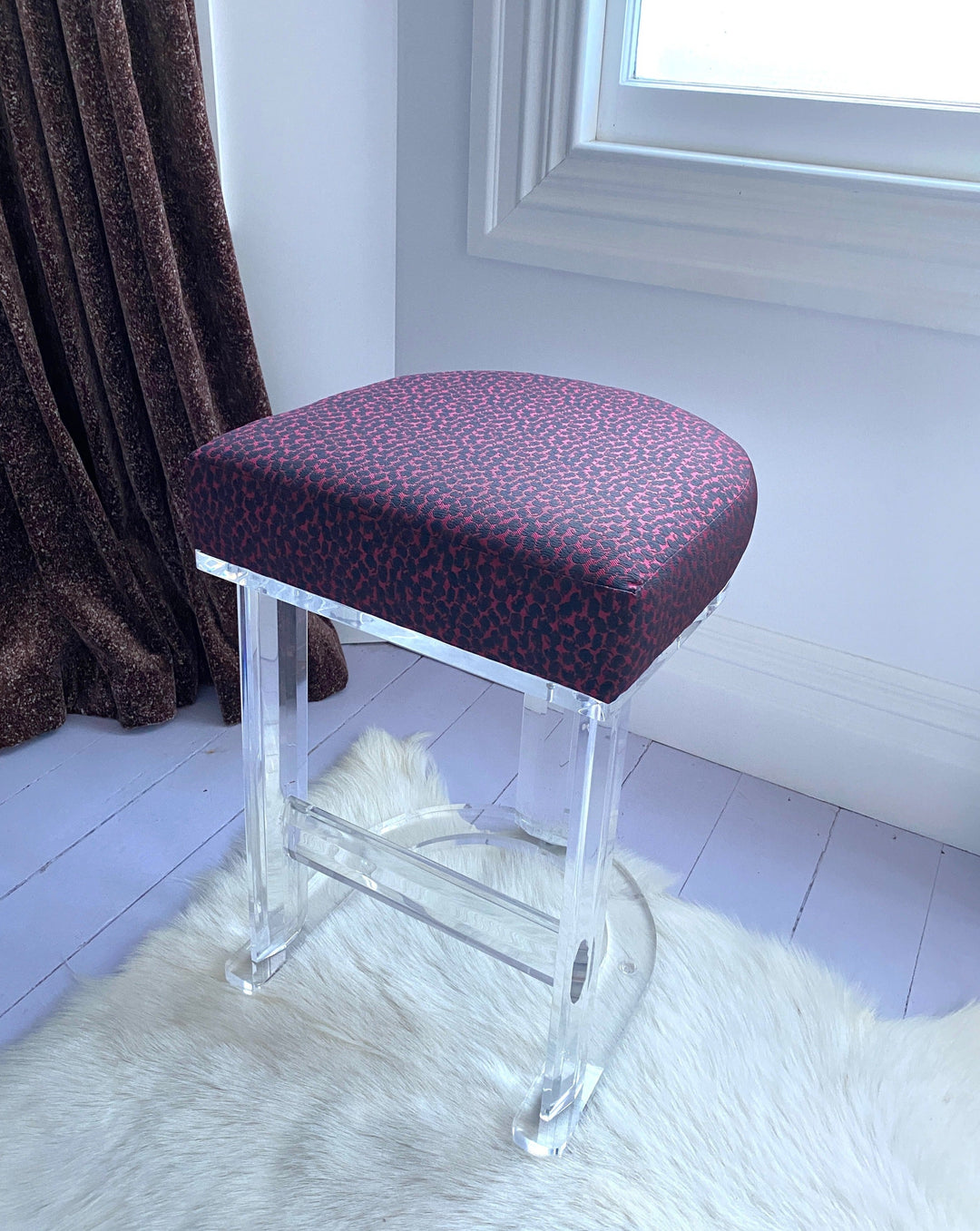 Upholstered bar stool with lucite frame by Vintage, featuring a red and black abstract pattern, over a faux fur rug.
