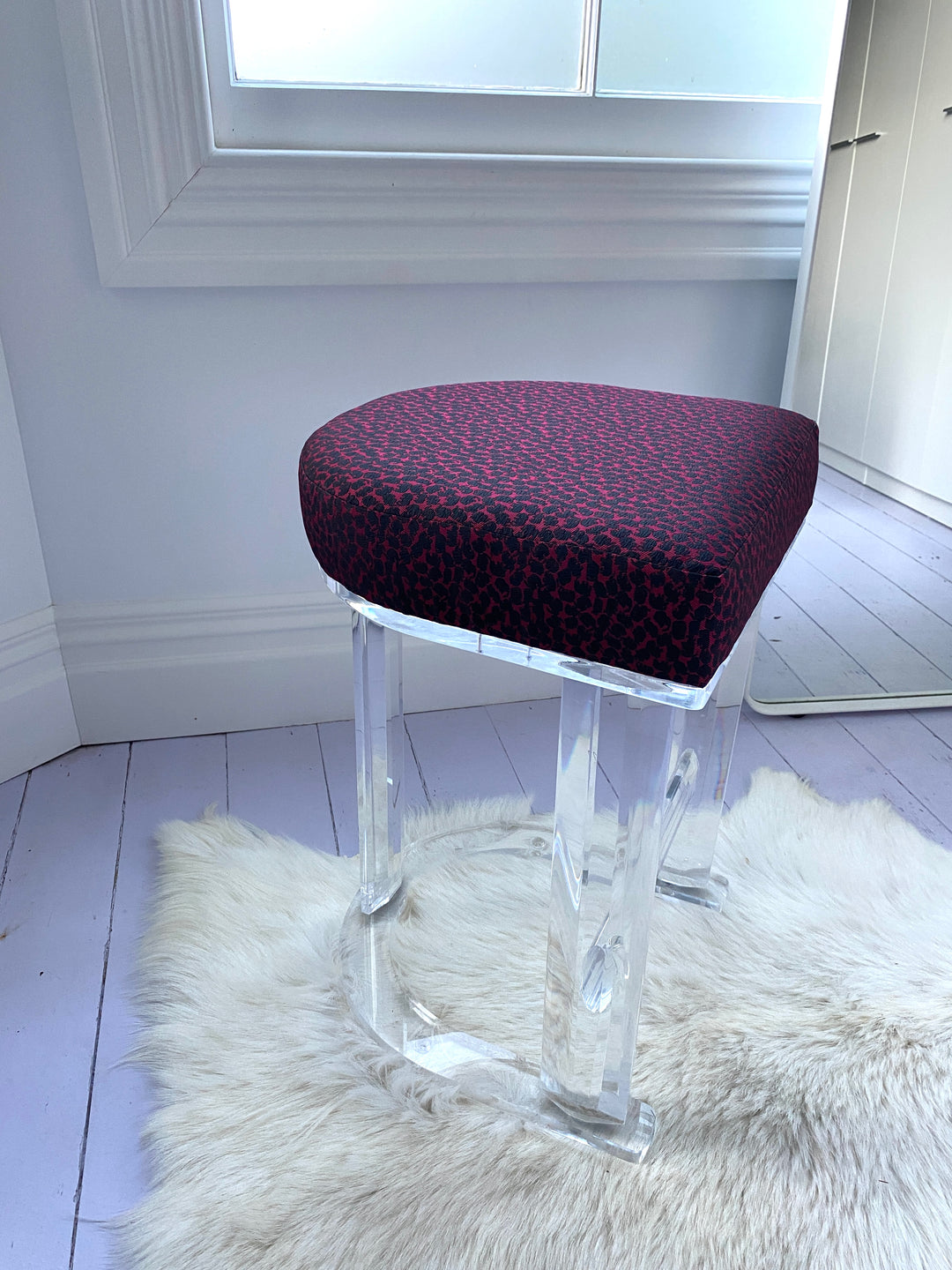 Upholstered vintage stool with clear lucite frame, standing on a cream shag rug.