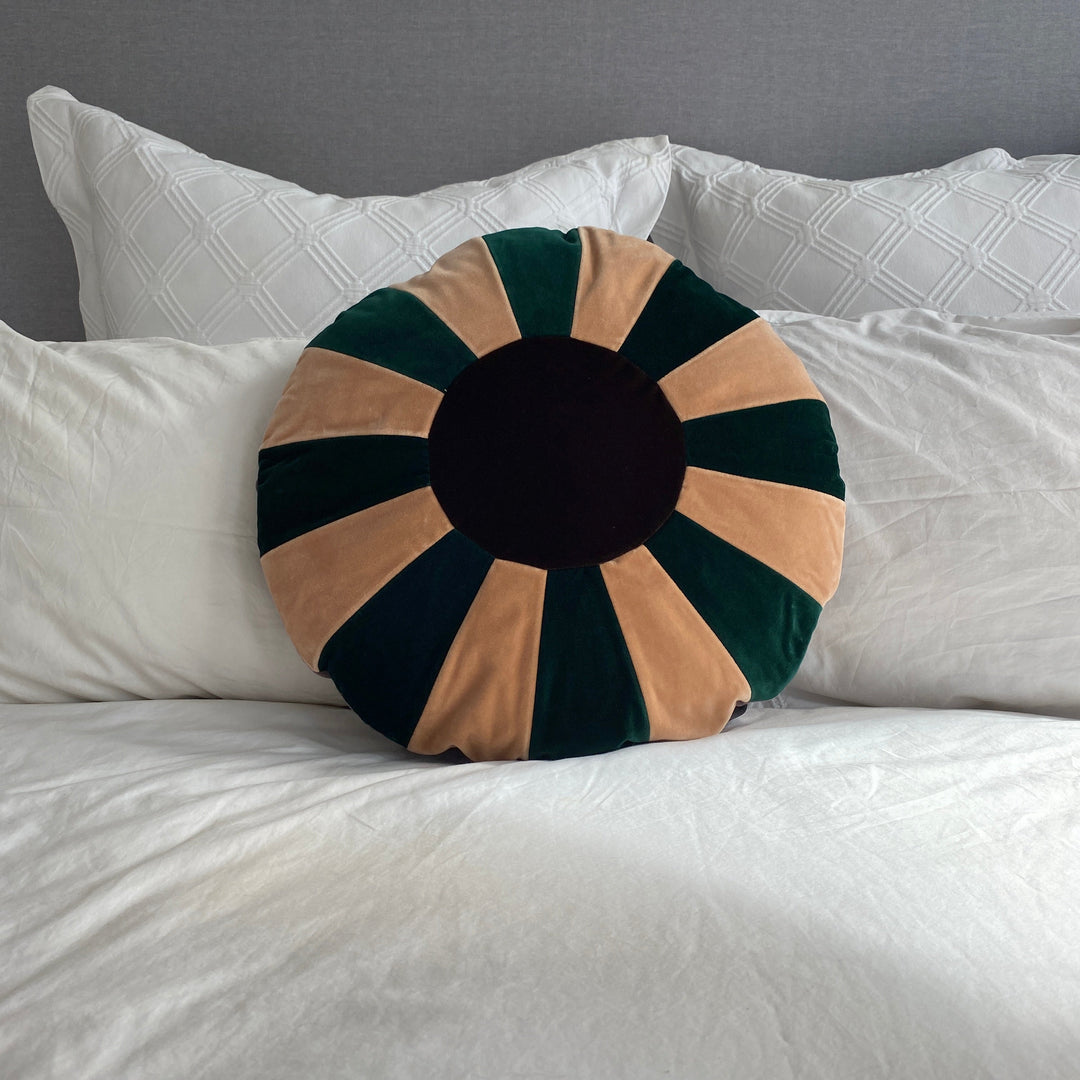 A round cushion with a green velvet cover on a bed, with a removable beige cotton cover visible in the center.