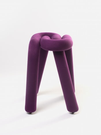 Purple velvet stool by Moustache Paris with a knotted top and cylindrical legs.