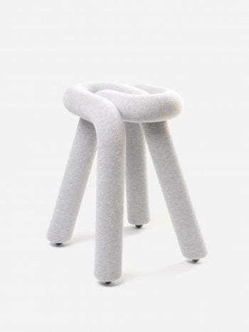 Light gray stool by Moustache Paris with a knot-like seat, covered in a textured fabric, and three rounded legs.
